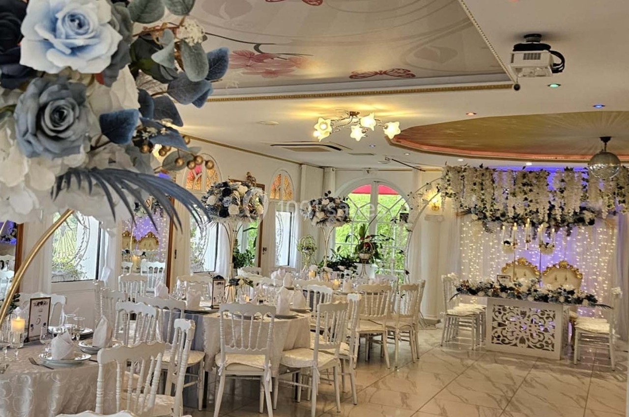 Salle de réception élégante décorée de fleurs blanches et bleues, avec tables dressées et éclairage tamisé.