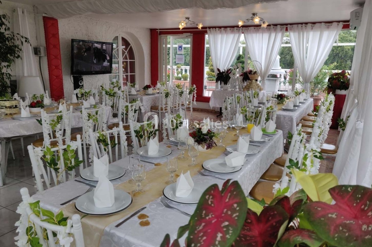 Salle de réception décorée avec des tables dressées, nappes blanches, serviettes pliées et arrangements floraux.