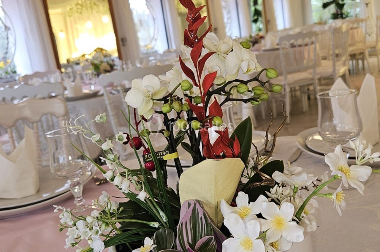 Location salle Athis-Mons (Essonne) - La Bella Vita #42 Centre de table floral avec des orchidées blanches et rouges, entouré de vaisselle sur une table de réception élégante.