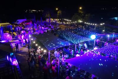Salle avec un bar, tables hautes et éclairage violet, grandes fenêtres ouvertes sur une terrasse.