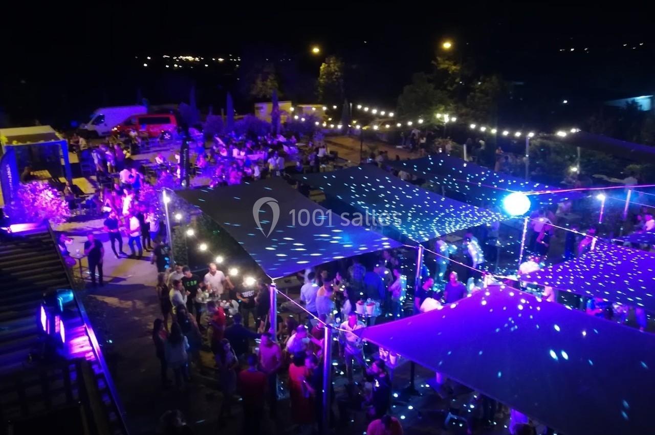 Vue nocturne d'une fête en plein air avec des lumières colorées, une piste de danse et des participants rassemblés.