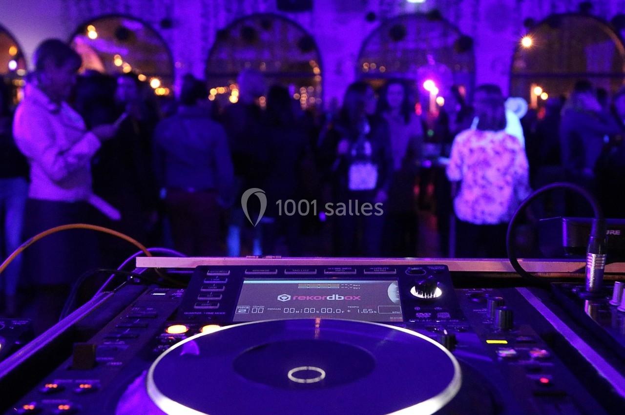 Platines de DJ en gros plan avec une foule dansante en arrière-plan sous des lumières tamisées.