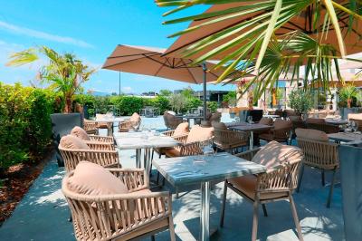 Salle avec un bar, tables hautes et éclairage violet, grandes fenêtres ouvertes sur une terrasse.