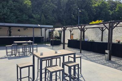 Salle avec un bar, tables hautes et éclairage violet, grandes fenêtres ouvertes sur une terrasse.