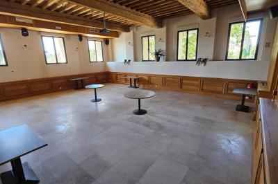 Salle avec un bar, tables hautes et éclairage violet, grandes fenêtres ouvertes sur une terrasse.