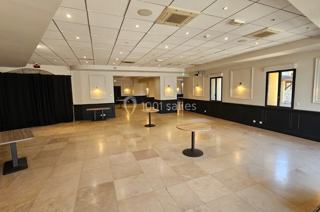 Salle lumineuse avec sol en carrelage clair, murs blancs, éclairage mural et tables rondes espacées.