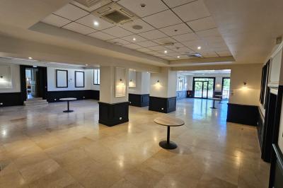 Salle avec un bar, tables hautes et éclairage violet, grandes fenêtres ouvertes sur une terrasse.