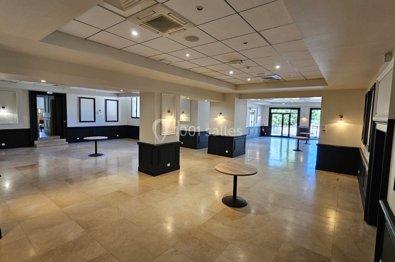 Salle spacieuse avec sol en marbre, murs clairs, éclairage encastré et quelques tables rondes dispersées.