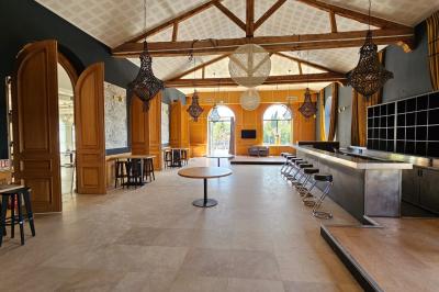 Salle avec un bar, tables hautes et éclairage violet, grandes fenêtres ouvertes sur une terrasse.