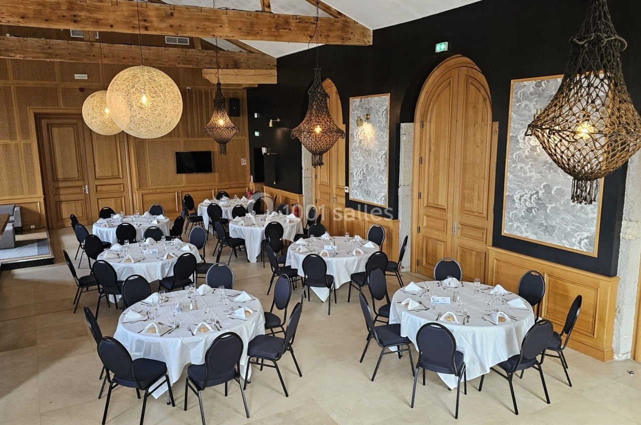 Salle de réception élégante avec tables rondes dressées, chaises noires et luminaires suspendus en osier.