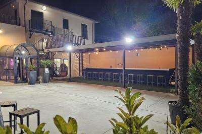 Salle avec un bar, tables hautes et éclairage violet, grandes fenêtres ouvertes sur une terrasse.