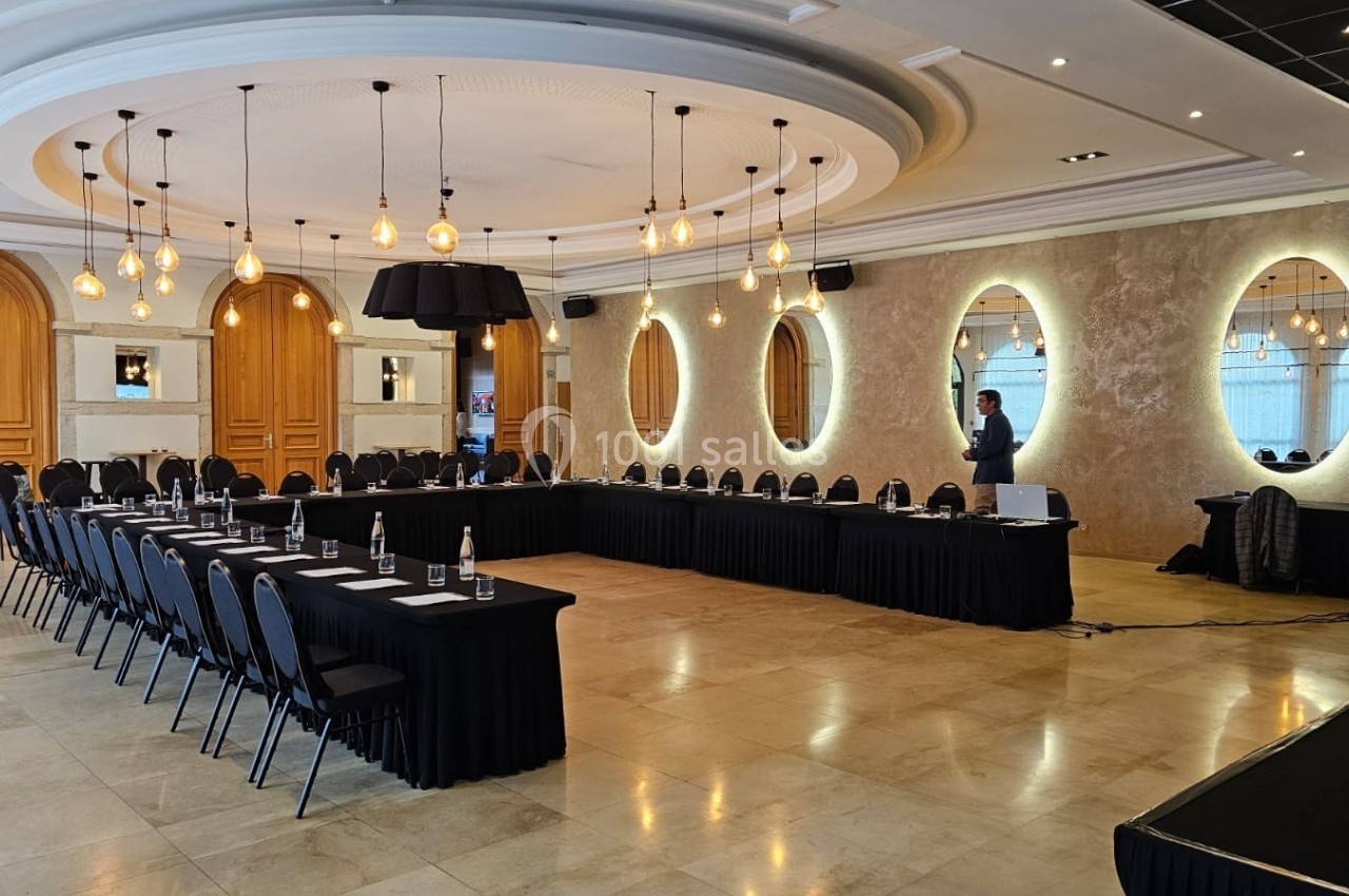 Salle de conférence élégante avec tables en U, chaises noires, éclairage suspendu et miroirs décoratifs sur les murs.