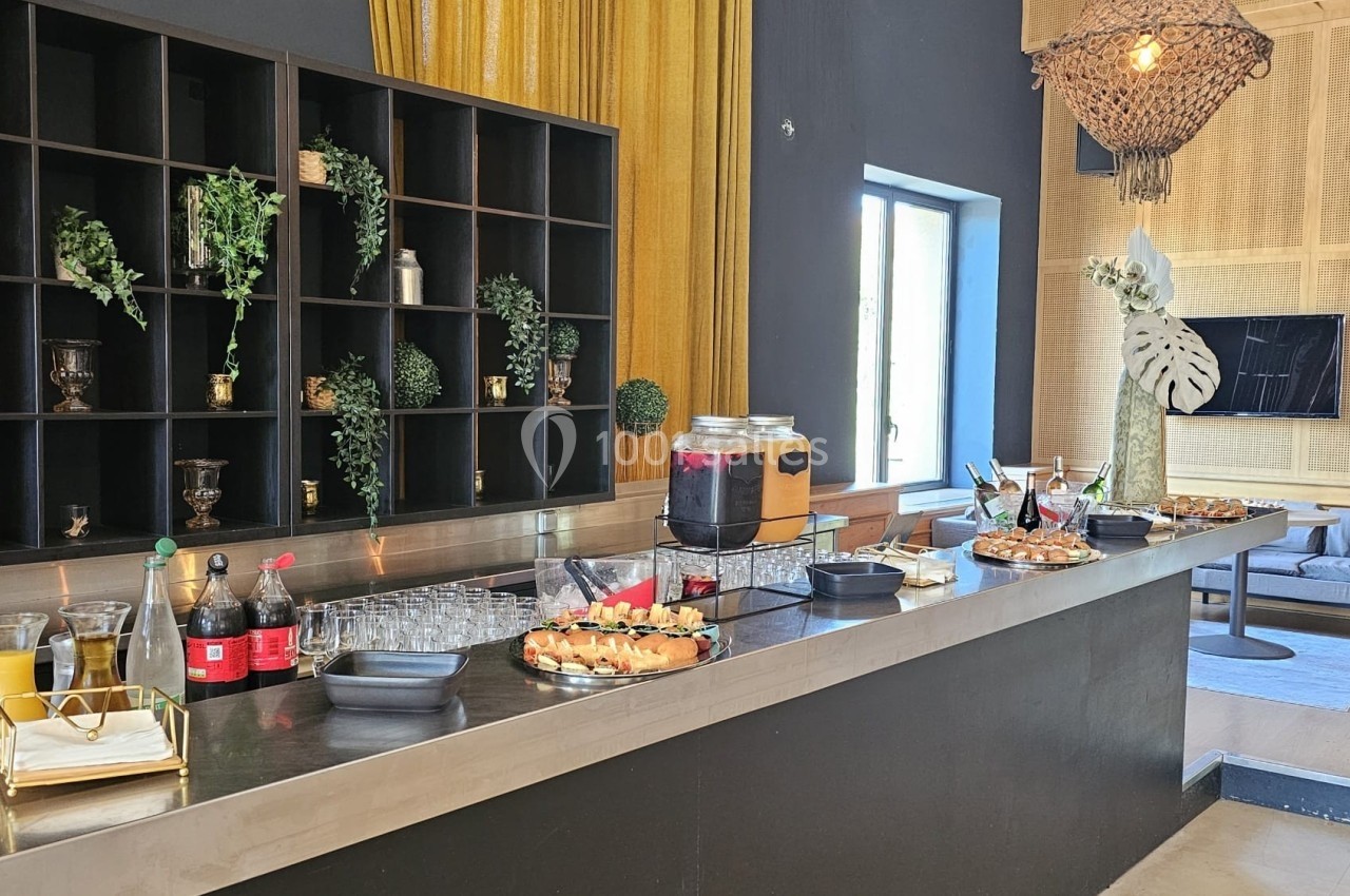 Buffet avec boissons, verrines et snacks disposés sur un comptoir moderne, décoré de plantes et éclairé naturellement.
