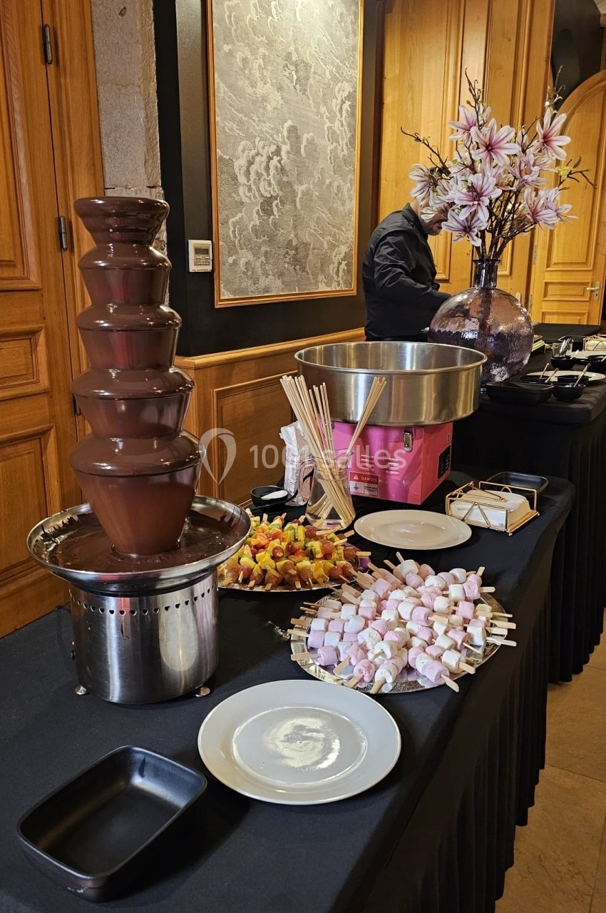 Fontaine de chocolat avec brochettes de fruits et guimauves disposées sur une table de buffet élégante.