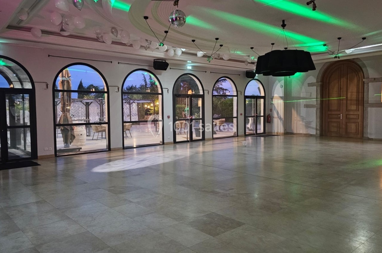 Salle spacieuse avec sol en marbre, grandes fenêtres cintrées et éclairage vert, donnant sur une terrasse extérieure.
