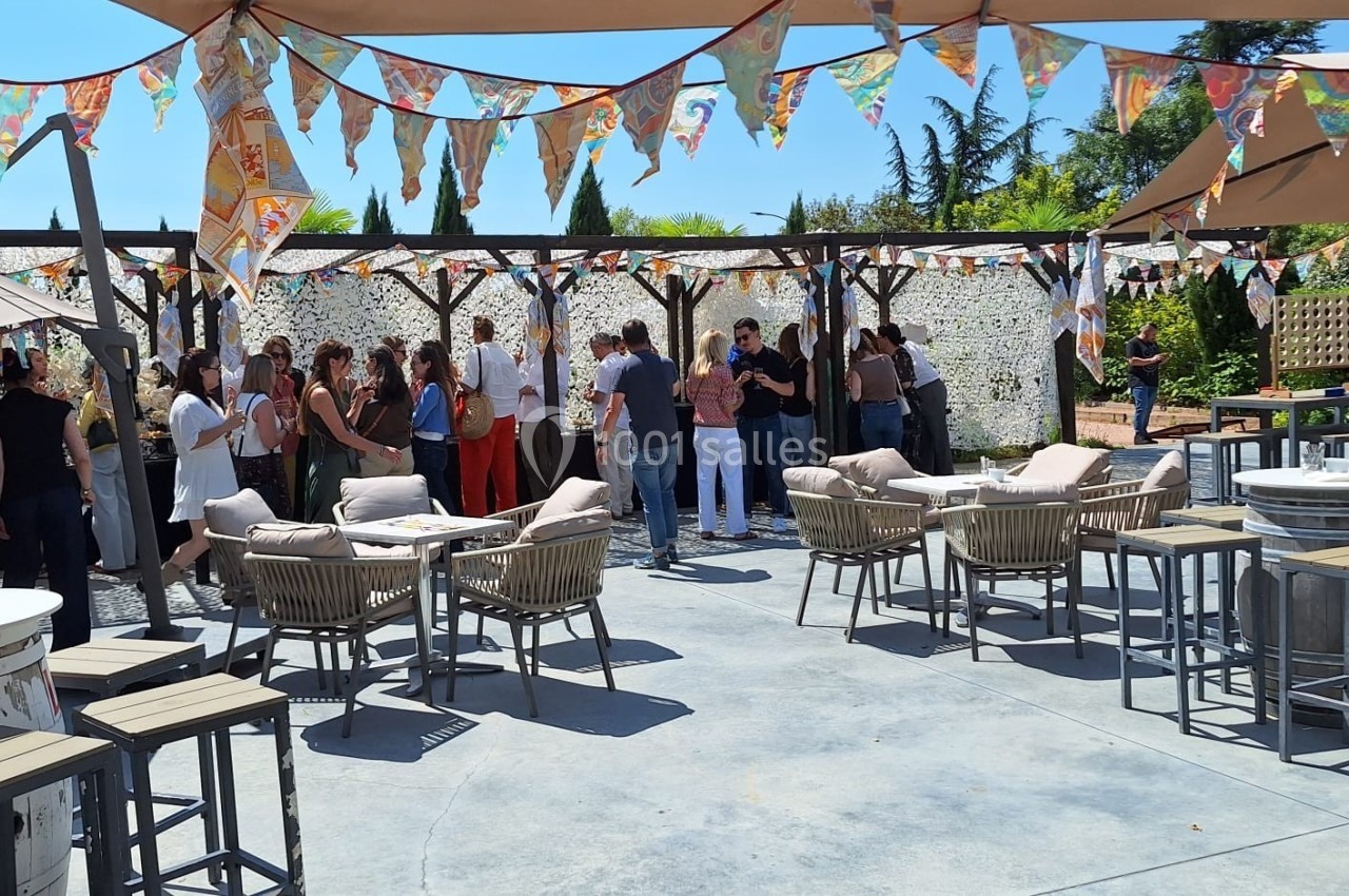 Personnes rassemblées dans un espace extérieur décoré de fanions colorés, avec tables et chaises sous des parasols.