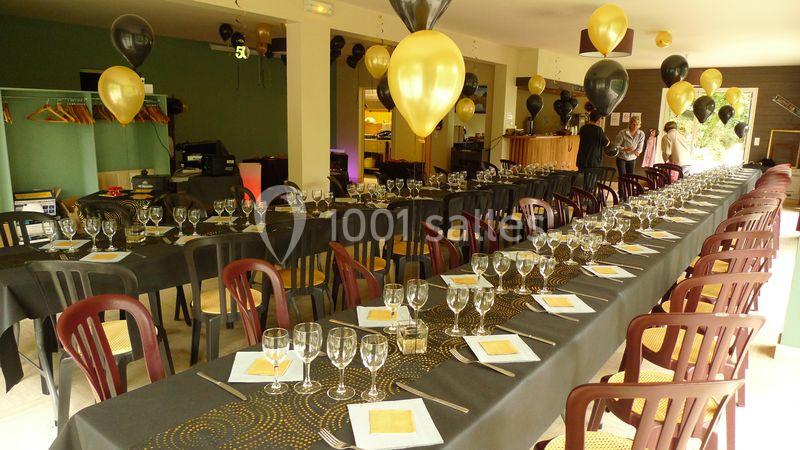 Salle décorée pour un événement avec de longues tables dressées, nappes noires et ballons noirs et dorés.