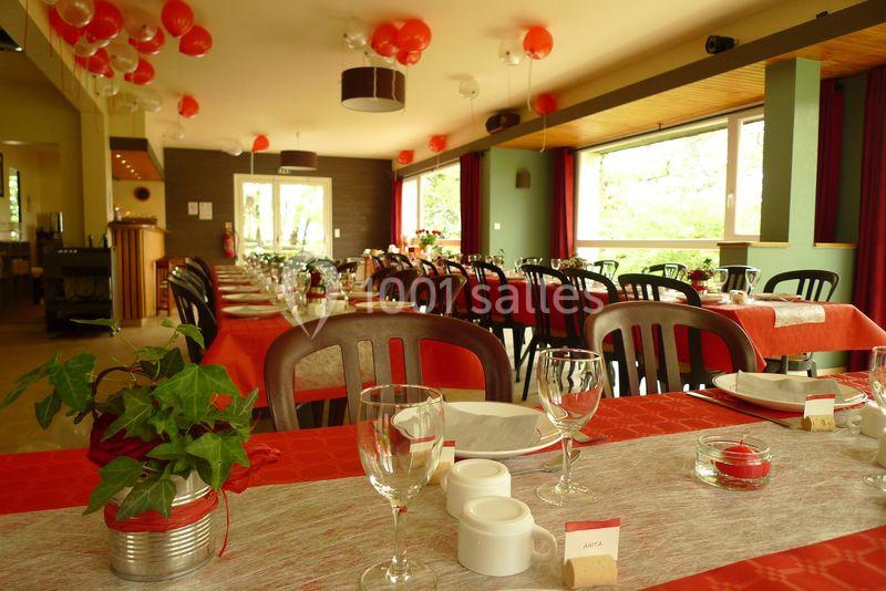 Salle de réception lumineuse avec tables dressées, nappes rouges et décorations suspendues en ballons rouges.