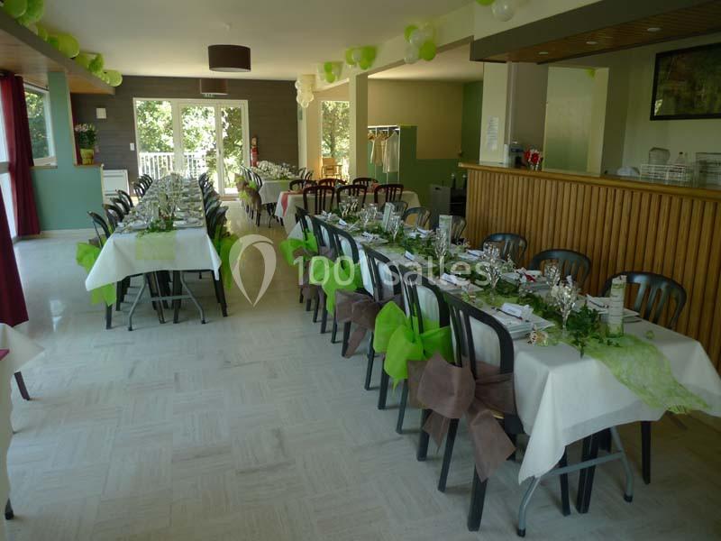 Salle décorée pour un événement avec des tables alignées, nappes blanches, chaises noires et ornements verts.