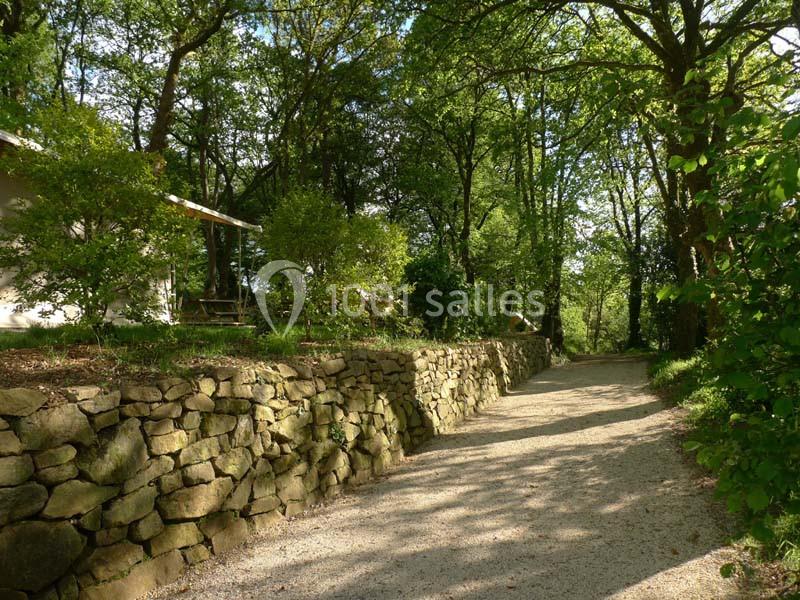 Chemin de gravier bordé de murs en pierre et d'arbres dans un cadre verdoyant.