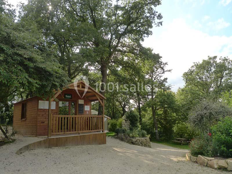 Cabane en bois entourée d'arbres dans un cadre naturel, avec une terrasse et un chemin en gravier menant à l'entrée.