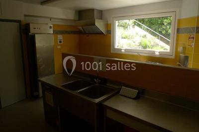 Cuisine professionnelle avec murs jaunes, plan de travail en inox, évier, cuisinière, fenêtre et équipements de rangement.