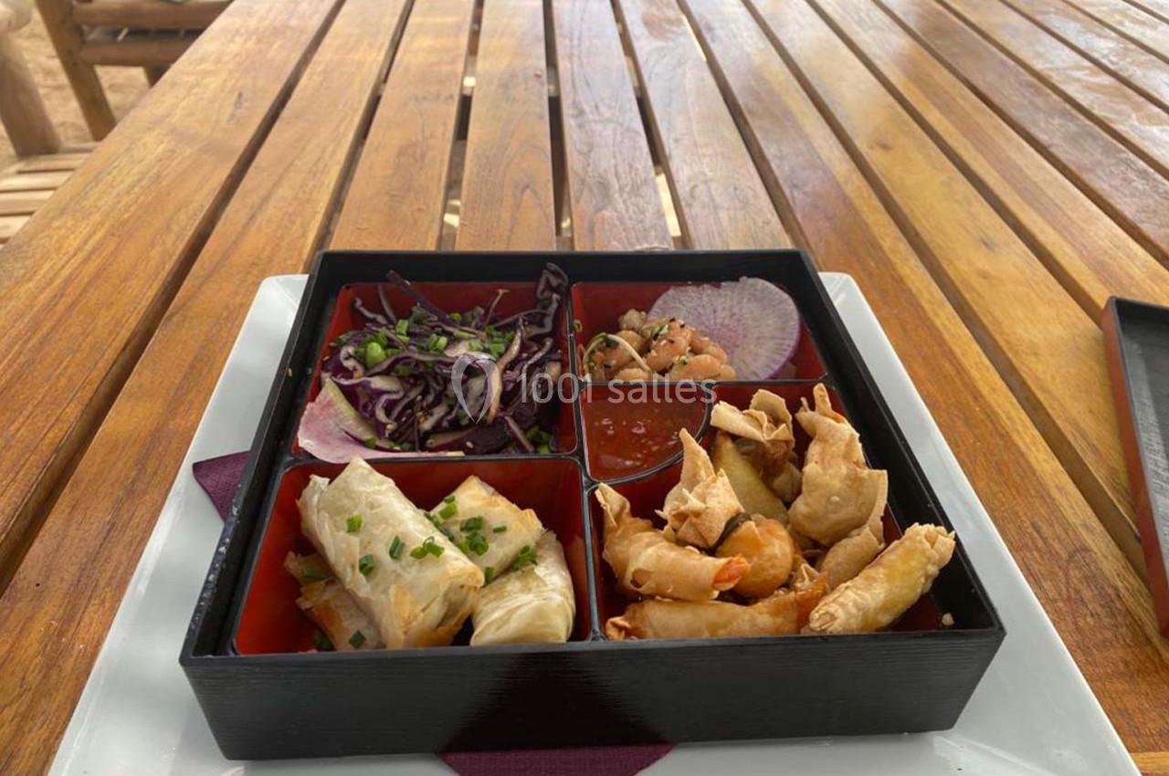 Plateau compartimenté contenant des rouleaux de printemps, crevettes frites, salade de chou rouge et sauce.