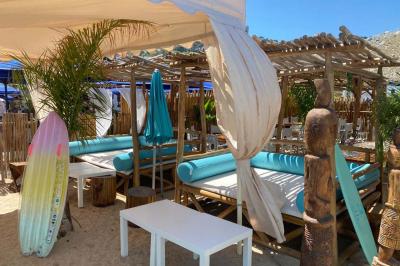 Bouteilles de vin rosé sur glace devant des parasols blancs et bleus sous un ciel dégagé.