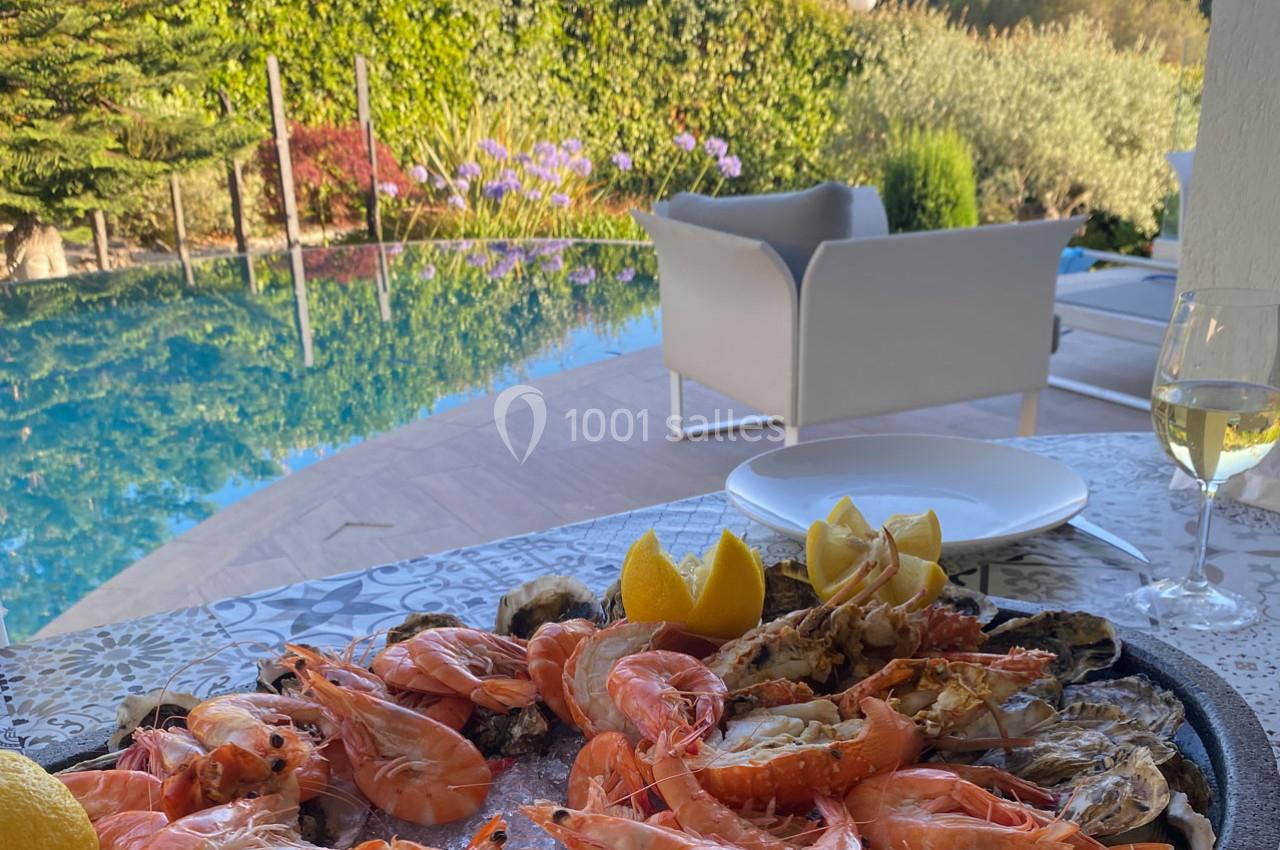 Plateau de fruits de mer avec crevettes et huîtres sur une table près d'une piscine entourée de végétation.