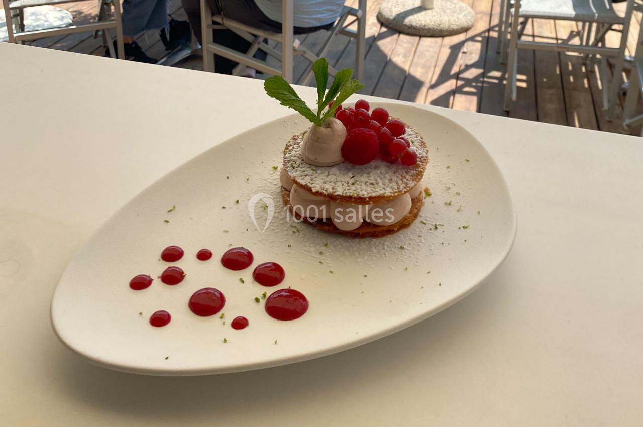 Dessert composé de framboises, crème et feuilles de menthe, présenté sur une assiette blanche avec coulis rouge.