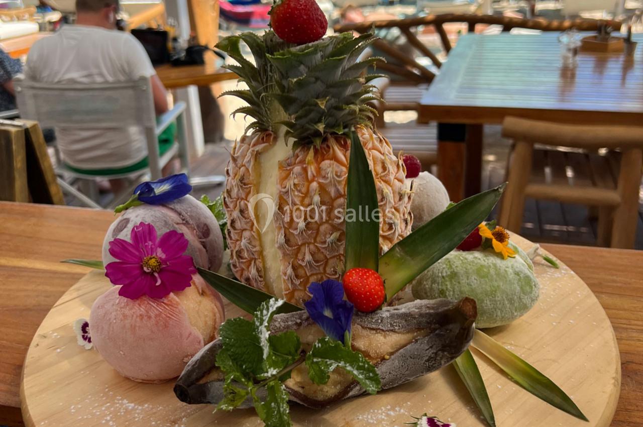 Ananas entier décoré de fleurs comestibles, fraises et mochi, présenté sur une planche en bois.