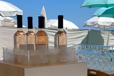 Bouteilles de vin rosé sur glace devant des parasols blancs et bleus sous un ciel dégagé.