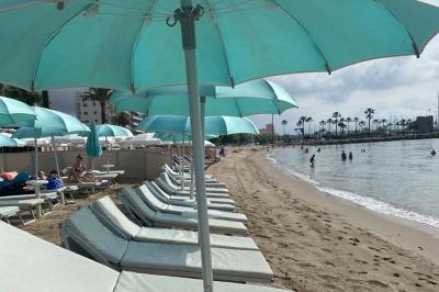 Bouteilles de vin rosé sur glace devant des parasols blancs et bleus sous un ciel dégagé.