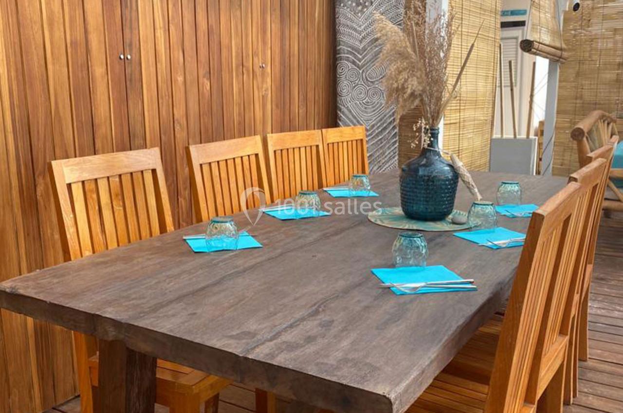 Table en bois avec six chaises assorties, décorée de serviettes bleues, verres et un vase avec des herbes séchées.