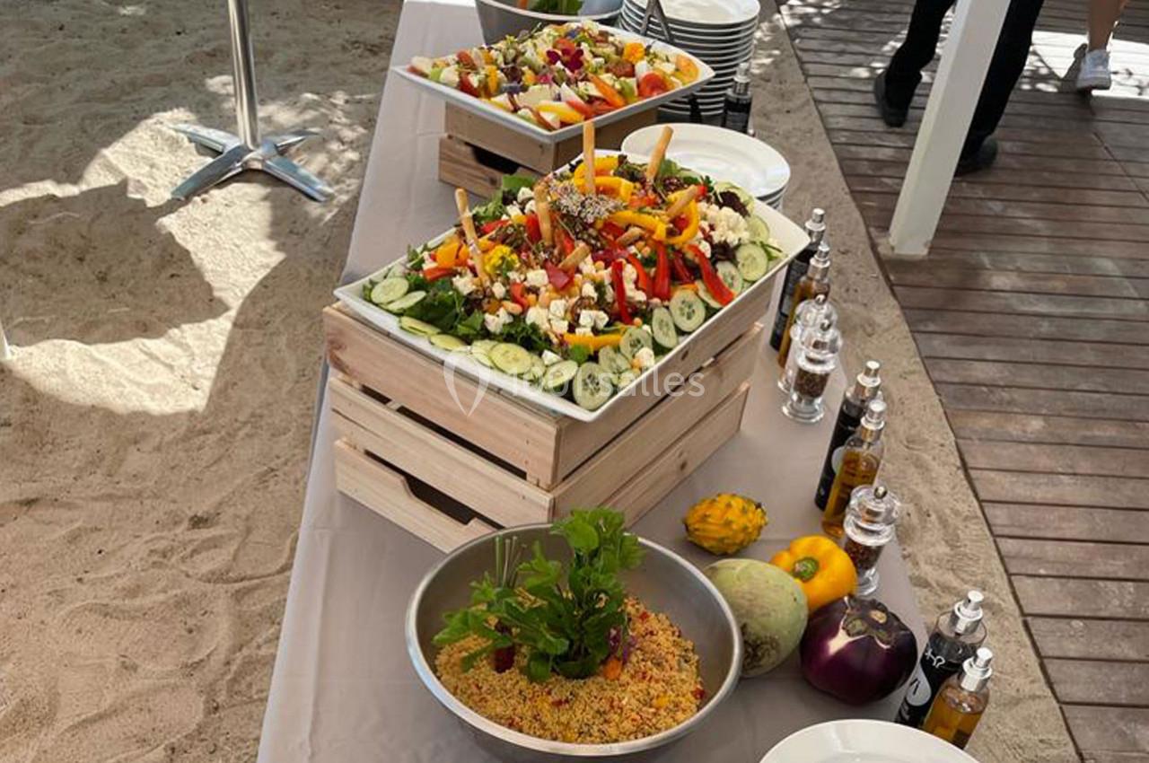 Buffet en extérieur avec salades colorées, légumes frais, couscous et condiments disposés sur une table en bois.