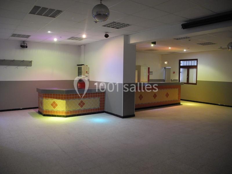 Salle vide avec un comptoir en carrelage décoratif, éclairée par des lumières colorées au plafond.