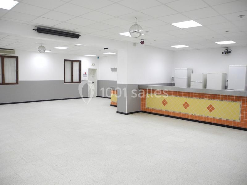 Salle vide avec sol clair, murs blancs et gris, comptoir carrelé orange et jaune, et plafond avec éclairage intégré.