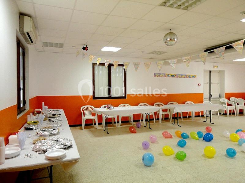 Salle décorée pour une fête avec guirlandes, ballons colorés au sol et tables dressées pour un buffet.