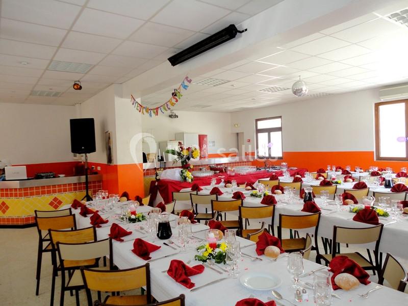 Salle décorée pour un événement, avec tables dressées, nappes blanches, serviettes rouges et guirlande festive.