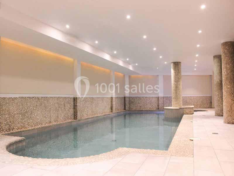 Piscine intérieure avec éclairage encastré, murs texturés et colonnes décoratives en pierre.