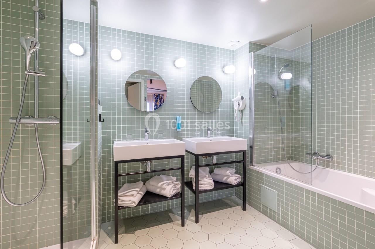Salle de bain moderne avec carrelage vert, deux lavabos, une baignoire, une douche et des miroirs ronds.