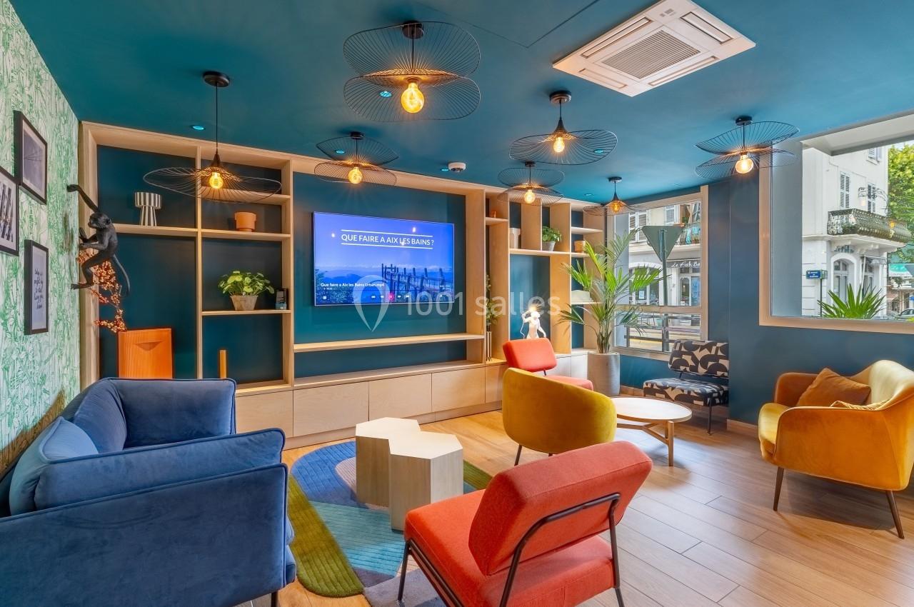 Espace lounge coloré avec fauteuils, tables basses, étagères décoratives et écran mural, éclairé par des suspensions…