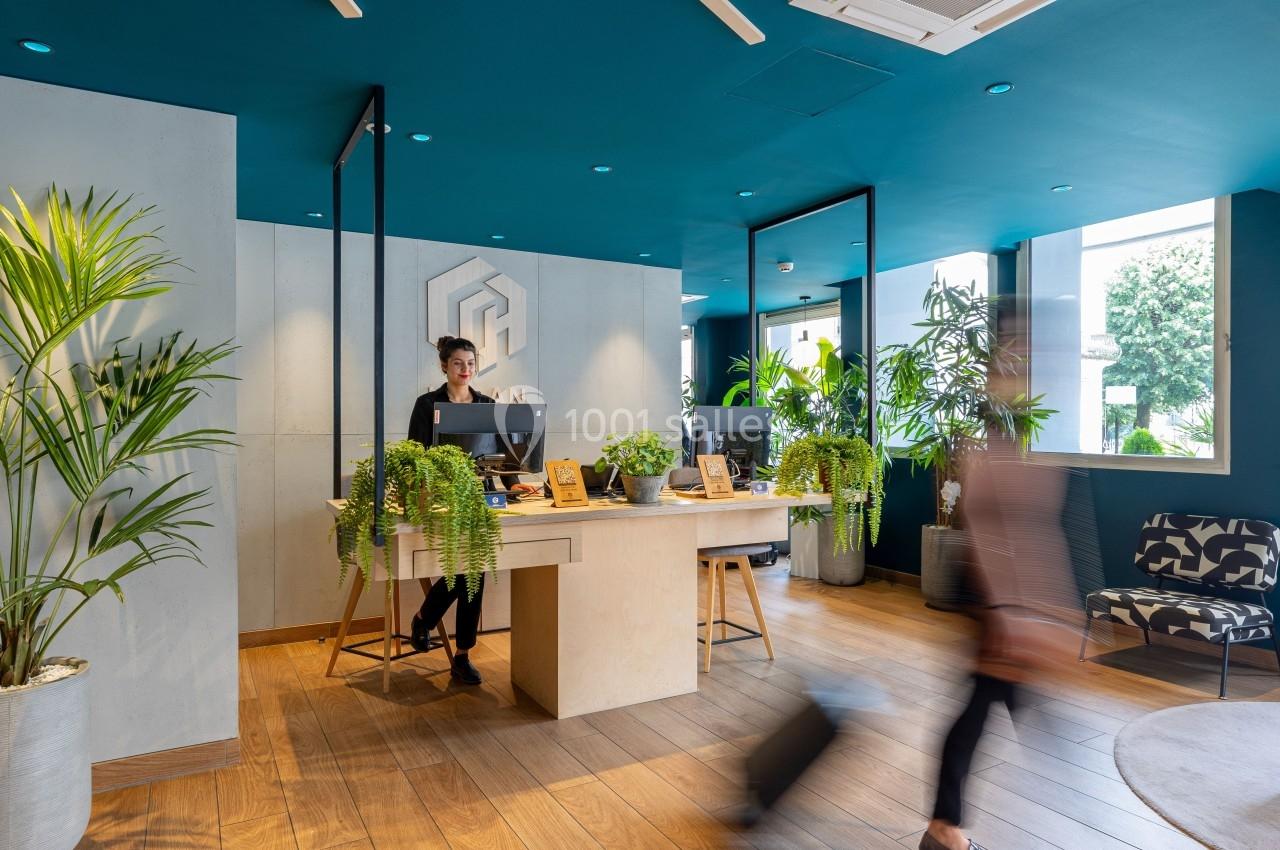 Accueil moderne avec comptoir en bois, plantes décoratives et une personne souriante dans un espace lumineux.