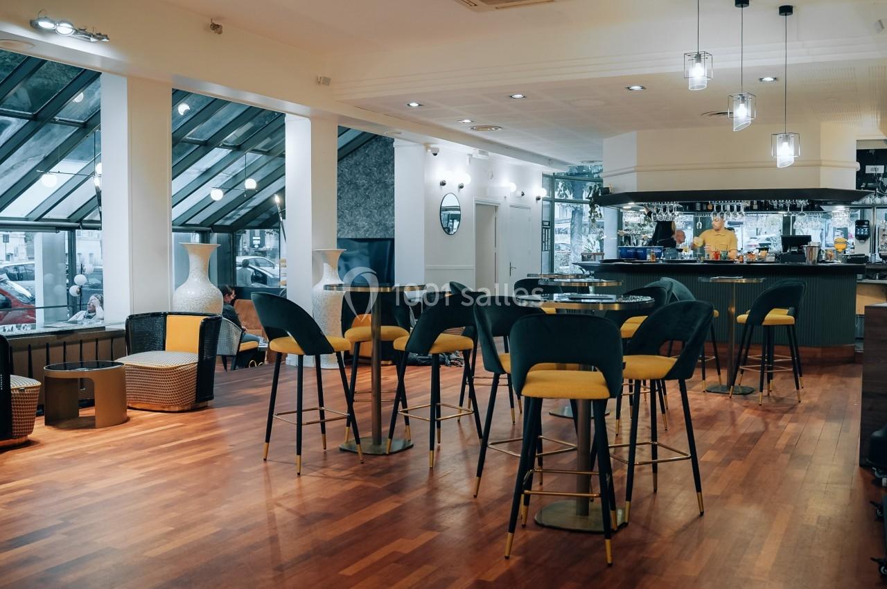 Salle de restaurant moderne avec parquet, chaises hautes, éclairage suspendu et vue sur l'extérieur à travers de grandes…