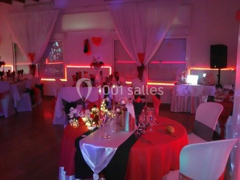 Salle de réception décorée avec des nappes rouges et blanches, éclairage tamisé et tables dressées pour un événement.