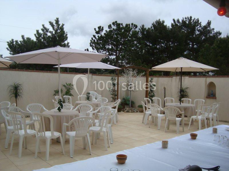 Terrasse aménagée avec des tables rondes, chaises blanches et parasols, entourée de murs et de végétation.