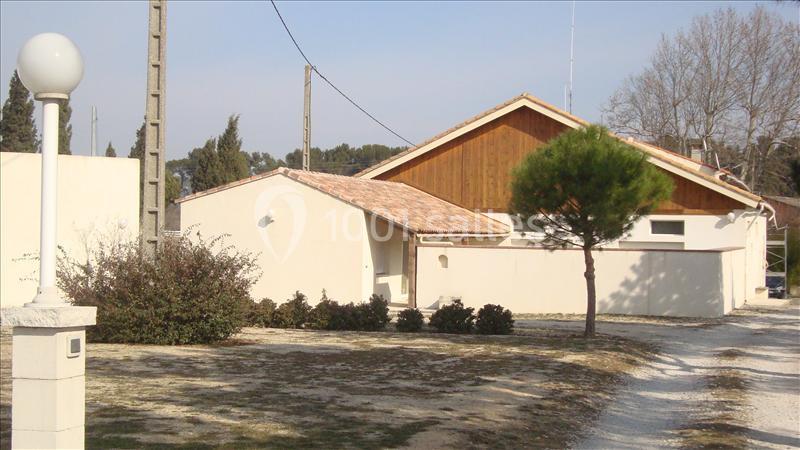 Maison avec façade claire, toit en tuiles, petit arbre au premier plan et chemin de gravier sur la droite.
