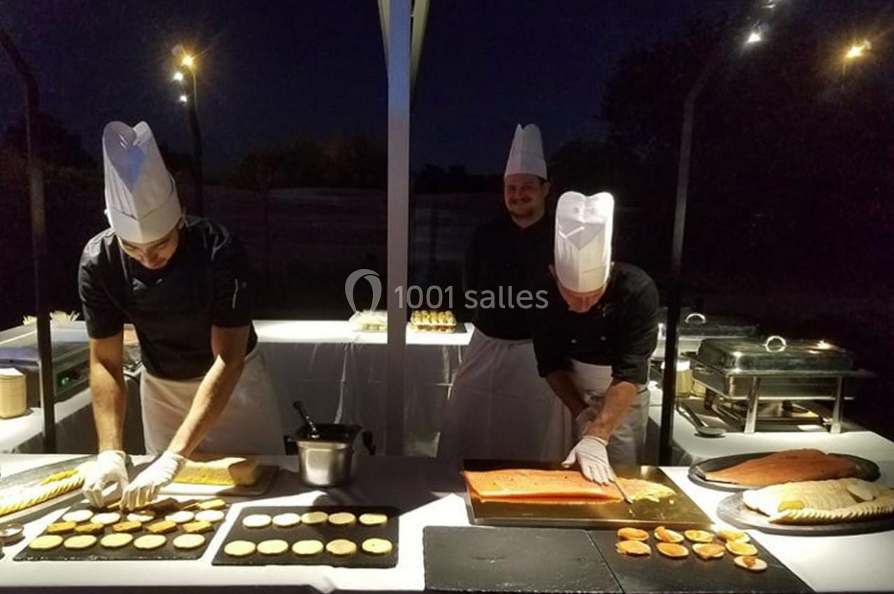 Des chefs cuisiniers préparent des plats sur des tables éclairées en extérieur, de nuit.