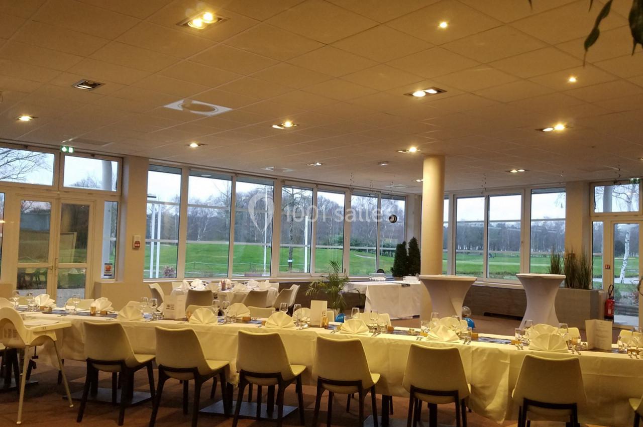 Salle de réception lumineuse avec grandes baies vitrées, tables dressées et vue sur un espace vert extérieur.
