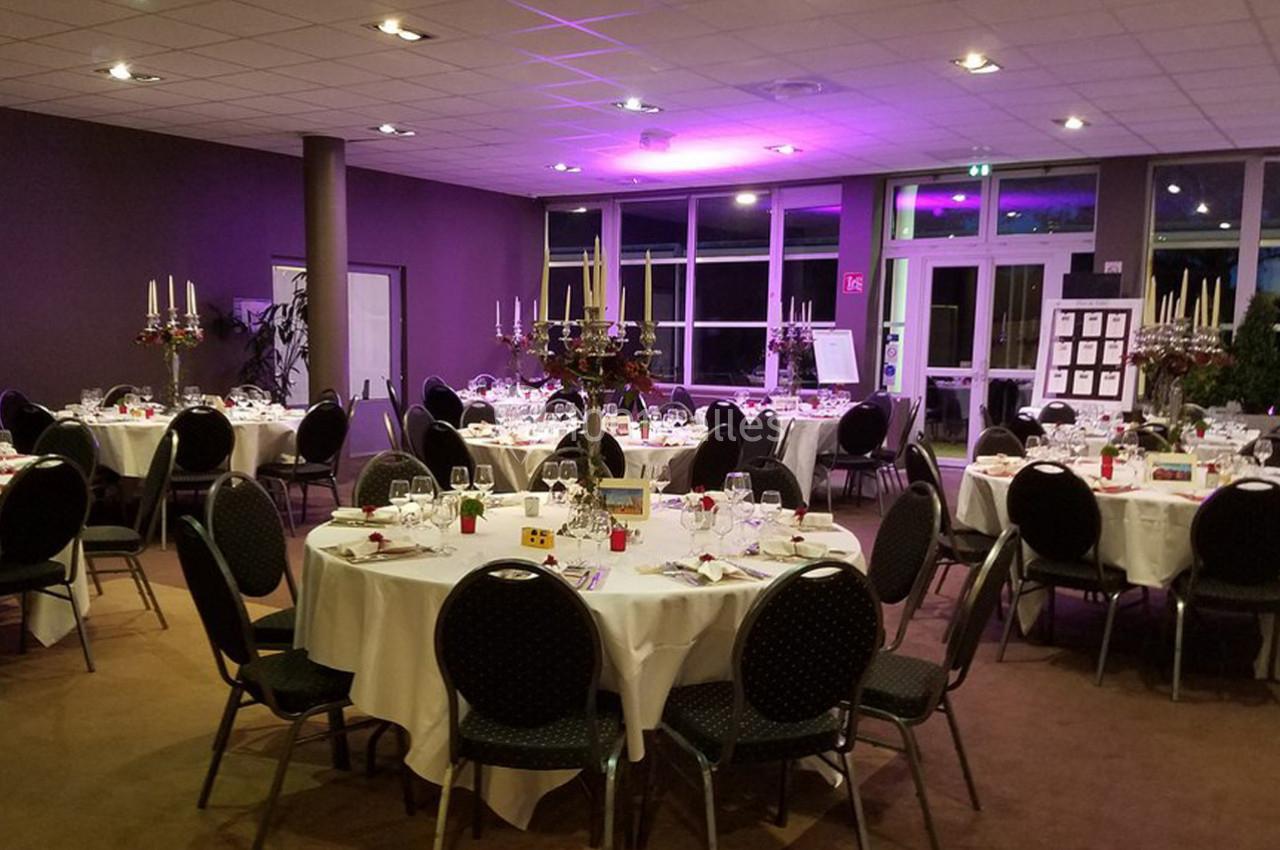 Salle de réception avec tables rondes dressées, chandeliers et éclairage d'ambiance violet.